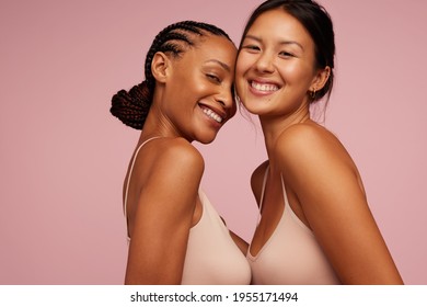 Two young women with different body type in underwear. Smiling females with glowing and radiant skin texture on pink background.