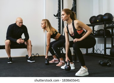 Two Young Women Doing Kettlebell Lifting. Crossfit Workout With A Personal Trainer Or Coach. Private Training Concept In A Small Private Sports Studio