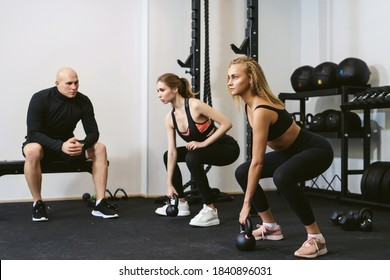 Two Young Women Doing Kettlebell Lifting. Crossfit Workout With A Personal Trainer Or Coach. Private Training Concept In A Small Private Sports Studio