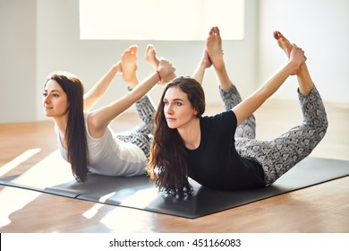 Two young women doing yoga asana bow pose. Dhanurasana - Powered by Shutterstock