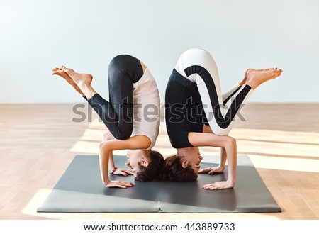 Two young women doing yoga asana crane pose. Bakasana