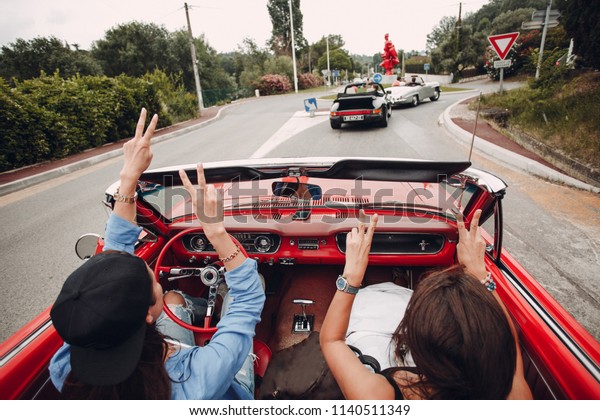 Two young\
women drive red cabriolet with hands up. Retro car rally. French\
riviera. Nice - Cannes -\
Saint-Tropez.