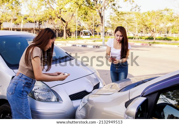 Two young women driving a car collide on a lane\
breaking traffic rules are using smartphones to take pictures\
together as evidence for car insurance claims : Accident and car\
insurance concept.