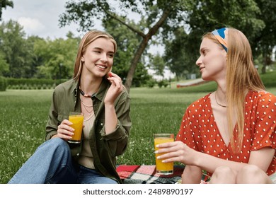 Two young women enjoy a picnic in a green park, sharing orange juice and conversation. - Powered by Shutterstock