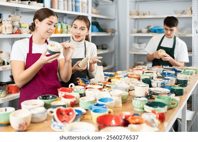 Two young women examining painted pottery in workshop - Powered by Shutterstock