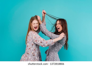 Two Young Women Fighting And Pulling Hair Isolated Over Turquoise Blue Background