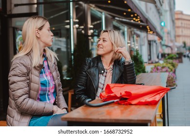 Two Young Women Friends Met In A City Street Cafe And Have Fun Chatting. Friendly Chance Meeting In Autumn