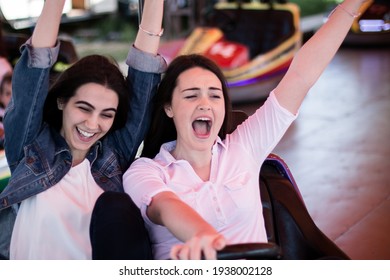 Two Young Women Having A Fun Bumper Car Ride At The Amusement Park In The Summer.