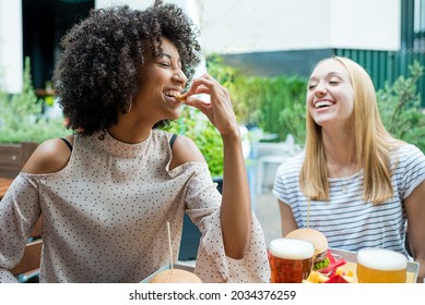 Two Young Women Having Fun While Eating Snacks At Restaurant, Group Of Multiethnic People Tasting Junk Food, Diversity And Inclusion Concept Of Multicultural Lifestyle