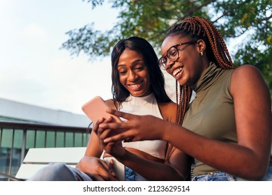 two young women having fun sitting on a park bench with a mobile phone, concept of youth and communication, copy space for text - Powered by Shutterstock