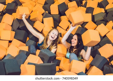 Two young women having fun with soft blocks at indoor children playground in the foam rubber pit in the trampoline center.