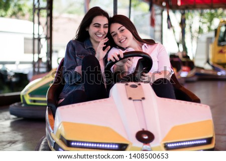 Two young women having a fun bumper car ride at the amusement park. Friendship.