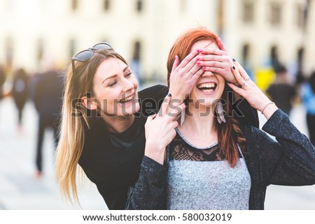 Two young women having fun together. Blonde girl playing peekaboo with her redhead friend. Happiness and lifestyle concepts, candid real people as models