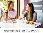 Two young women are having a snack in a modern cafe. The friends are having sweets, milkshakes and ice cream cups for dessert. Concept of friends meeting in a cafe and having sweets.