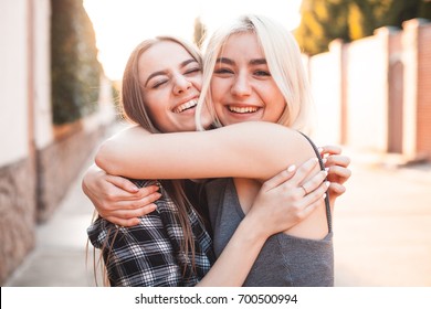 Two young women hugging and laughing at sunset in the city. Best friends