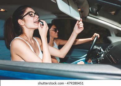 Two Young Women Inside The Car.They Are Driving The Car And Fixing Makeup.Preparing To Go Out.Clubbing And Nightlife.