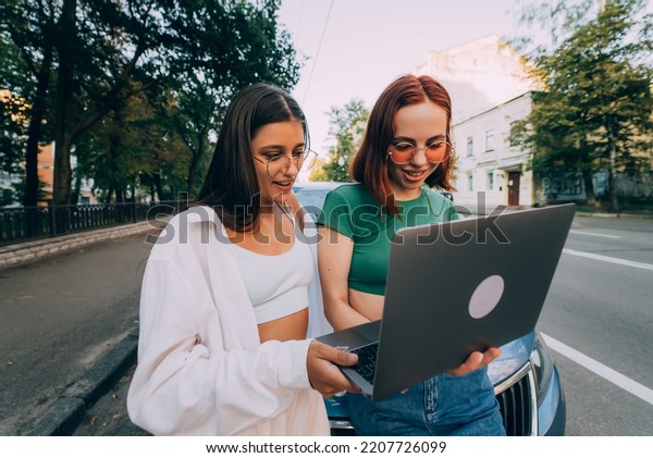 Two young women\
with a laptop near the car