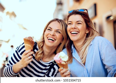 Two Young Women Laughing And Holding Ice Cream In Hand