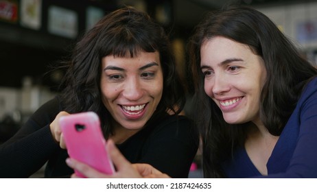 Two Young Women Looking At Smartphone Device Screen Smiling. Female Friends Sharing Information Watching Content Online