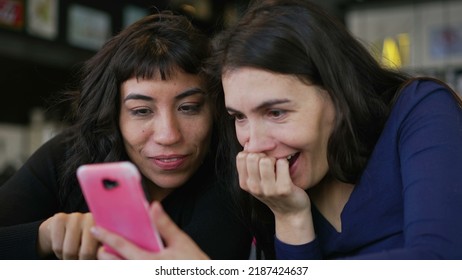 Two Young Women Looking At Smartphone Device Screen Smiling. Female Friends Sharing Information Watching Content Online