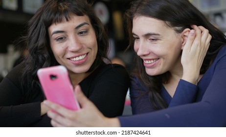 Two Young Women Looking At Smartphone Device Screen Smiling. Female Friends Sharing Information Watching Content Online