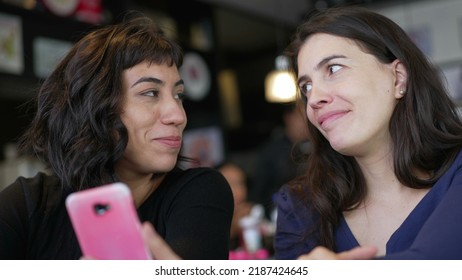 Two Young Women Looking At Smartphone Device Screen Smiling. Female Friends Sharing Information Watching Content Online