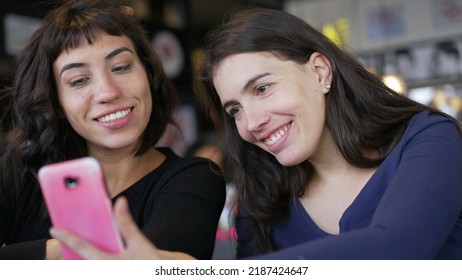 Two Young Women Looking At Smartphone Device Screen Smiling. Female Friends Sharing Information Watching Content Online