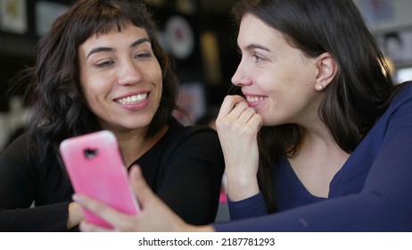 Two Young Women Looking At Smartphone Device Screen Smiling. Female Friends Sharing Information Watching Content Online