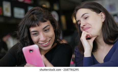 Two Young Women Looking At Smartphone Device Screen Smiling. Female Friends Sharing Information Watching Content Online