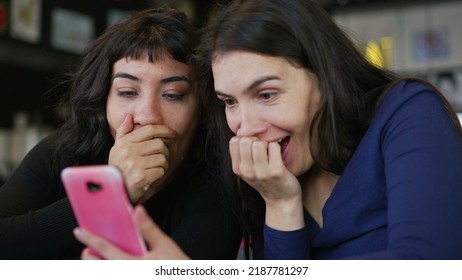 Two Young Women Looking At Smartphone Device Screen Smiling. Female Friends Sharing Information Watching Content Online