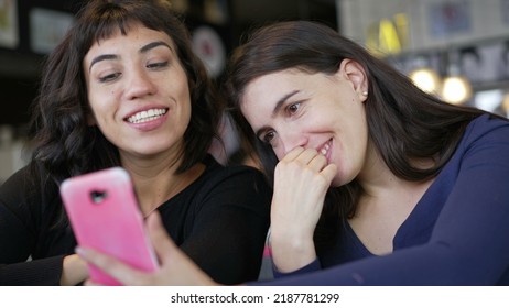 Two Young Women Looking At Smartphone Device Screen Smiling. Female Friends Sharing Information Watching Content Online