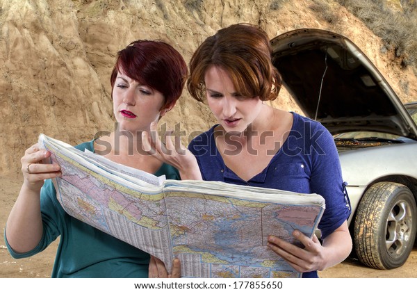 two young women are lost and looking at a map.\
broken car in the\
background