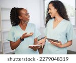 Two young women in the medical field wearing scrubs discuss with digital tablets