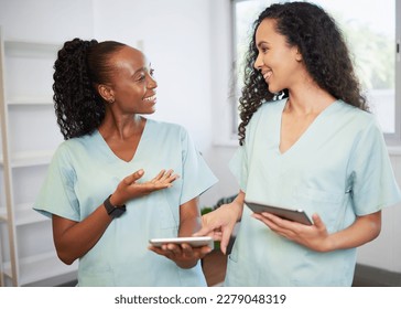 Two young women in the medical field wearing scrubs discuss with digital tablets - Powered by Shutterstock