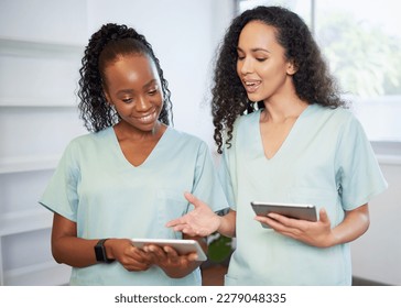 Two young women in the medical field wearing scrubs discuss with digital tablets - Powered by Shutterstock