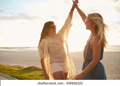 Two Young Women On The Beach Giving High Five. Women Friends Enjoying Beach Vacation.