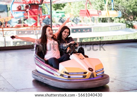 Two young women on a fun bumper car ride together at the amusement park in the summer.