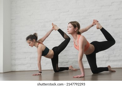 Two Young Women Practicing Stretching Yoga Positions In Yoga Studio. Wellbeing And Self Care Concept.