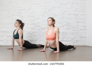 Two Young Women Practicing Stretching Yoga Positions In Yoga Studio. Wellbeing And Self Care Concept.