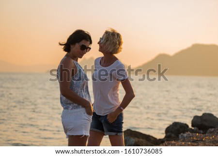 Two young women in profile on a sunset background by the sea
