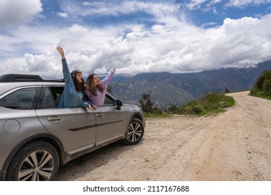 Two Young Women Protruding From A Car Window With The Arms Raised Gesturing Freedom In The Mountains