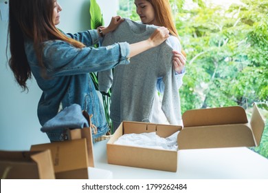 Two Young Women Receiving A Postal Parcel Box And Try On Clothes At Home For Delivery And Online Shopping Concept