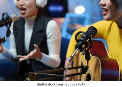 Two young women are recording music in a professional sound studio, one singing and the other playing acoustic guitar - Powered by Shutterstock