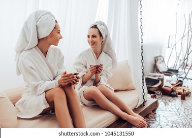 Two young women are relaxing in spa and wellness center. Talking and drinking tea together. - Powered by Shutterstock