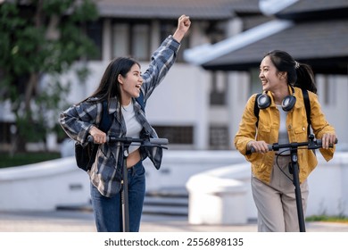 Two young women riding scooters and smiling. One of them is wearing a yellow jacket. Scene is happy and carefree - Powered by Shutterstock