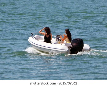 
Two Young Women Riding In A Small Sporty White Pontoon Motor Boat Powered By One Outboard Engine.