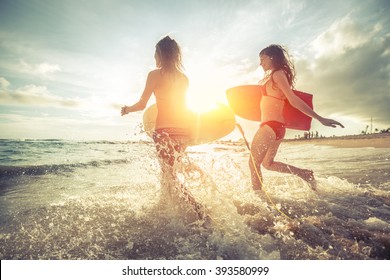 Two Young Women Running Into The Sea With Surf Boards