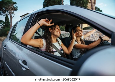 Two young women sing a song on the radio and dance in the car on a day trip in the summer - Best friends having fun together driving around the countryside - Smiling millennial in a relaxing moment - Shutterstock ID 2069862047