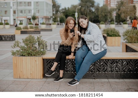 Two young women sit in a city Park with a phone