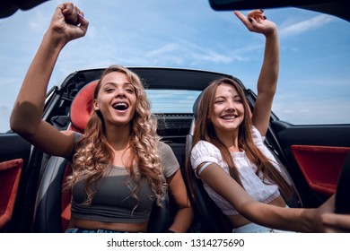 two young women sitting in the front seat of a convertible